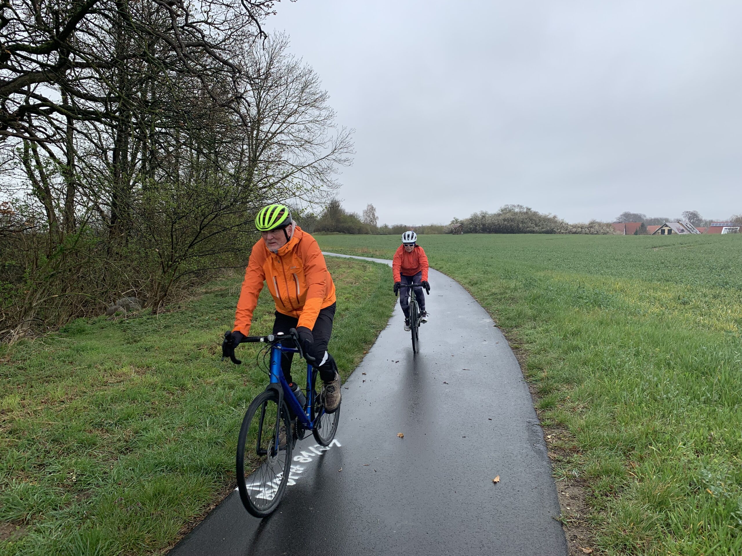 To syklister som kommer i mot oss på en sykkelvei. Det regner.